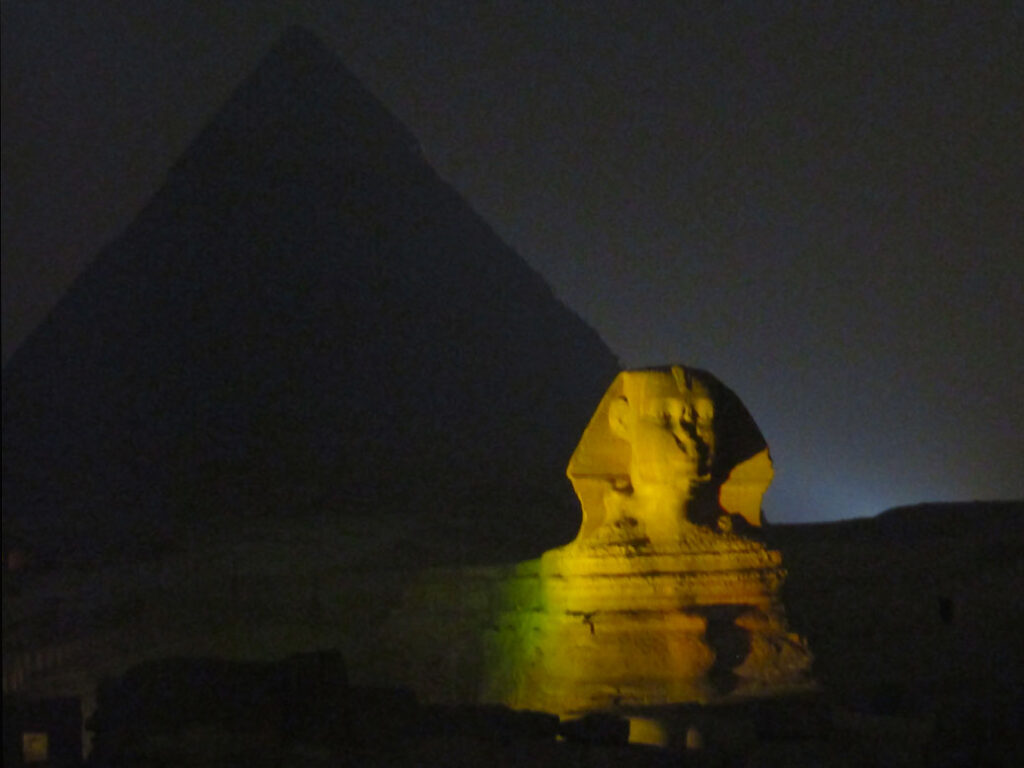 The illuminated Sphinx, with the body of a lion and the head of a person, is quite smaller than the pyramids but still impressive.